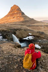 Adventurous photographer woman in winter in Iceland photographing sitting at Kirkjufell waterfall © xamnex