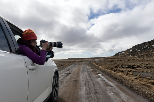 A woman takes a photo of a stunning Icelandic landscape. A tourist takes pictures with her camera during a trip to Iceland, stopping in her car.