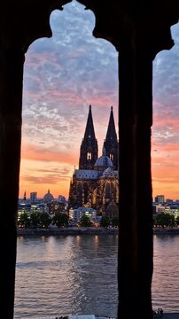 Cologne Cathedral Gothic Window Sunset River View - A dramatic silhouette of a gothic window frame perfectly frames a stunning sunset view of Cologne Cathedral and the Rhine River.