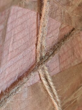 Extreme close-up of rough jute twine crisscrossing over textured pink paper packaging