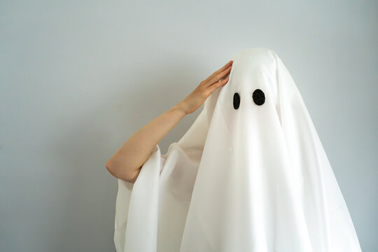 Funny ghost character wearing a classic white sheet costume and black eyes, posing with one hand on its head. Humorous Halloween and spooky season concept.