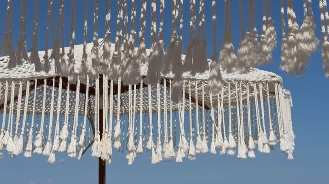 Delicate white macrame fringe tassels hang and sway gently against a bright clear blue sky