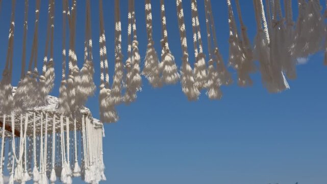 A close up view shows delicate white macrame fringe strands swaying gently in the wind
