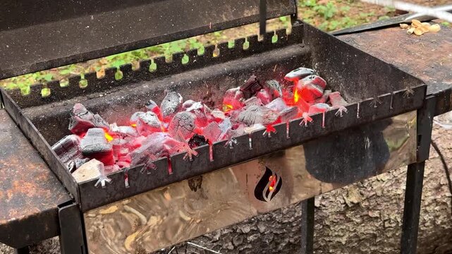 Hand of an adult stirring burning charcoal in a metal grill outdoors, barbecue preparation, outdoor cooking, summer picnic, campfire concept.