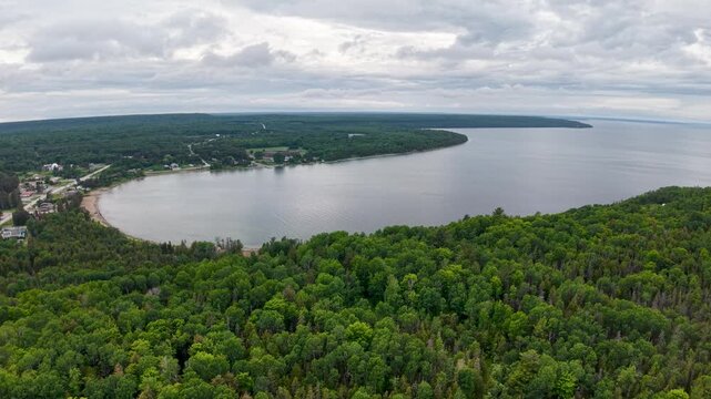 A scenic drone shot follows green vegetation forests and distant hills across Manitoulin Island beneath a bright cloudy sky