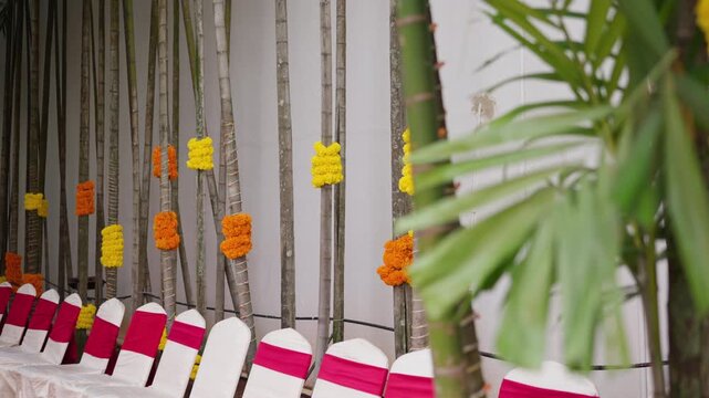Rows of decorated chairs and bamboo with marigold garlands at outdoor wedding venue