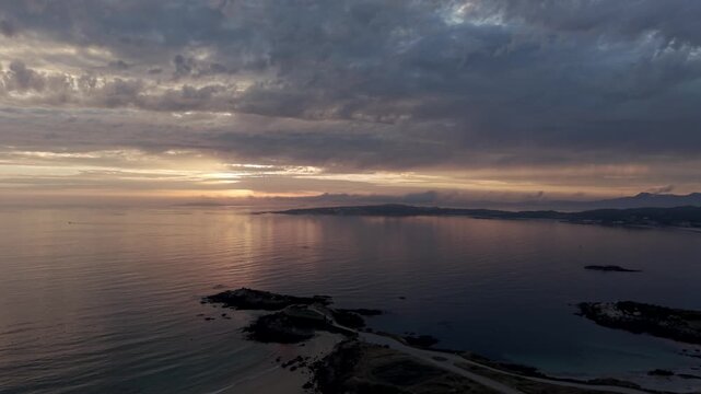 Aerial drone view of a moody sunset over the calm sea with soft light rocky reefs and layered clouds at A Lanzada beach in Galicia Spain