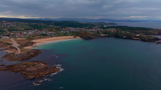 Aerial drone view of Paxos beach with rocky islets turquoise water and a coastal town near the Lanzada chapel in Sanxenxo Galicia Spain