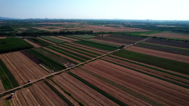 A high-angle aerial shot shows patchwork agricultural fields with field roads, under a clear sky in rural areas.