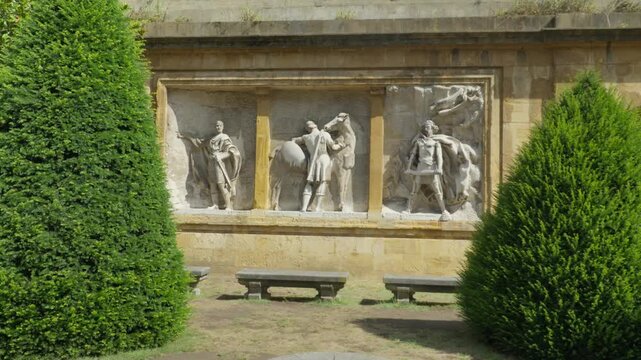 Wide shot of stone wall reliefs with medieval statues framed by green trees