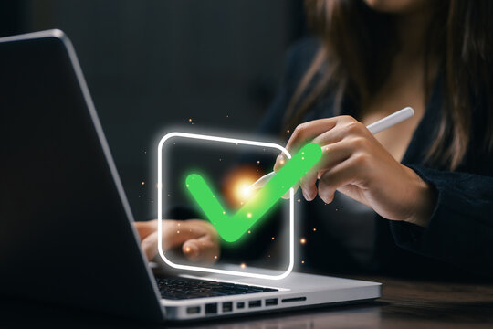 Businesswoman using a stylus to select a digital check mark on laptop, representing online approval, task completion, verification, quality control, compliance, and workflow management.