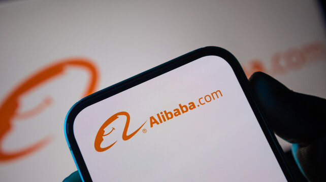 Alibaba com e-commerce platform logo on smartphone screen held by hand.