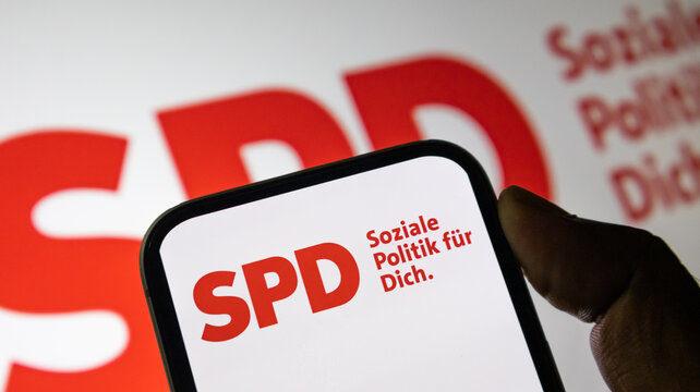 German SPD logo on mobile device screen against blurred political slogan backdrop.