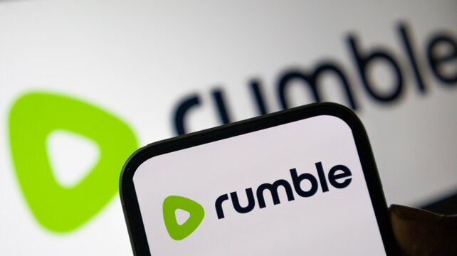 Rumble video platform logo featured on smartphone screen with brand signage background for content creators and social media.