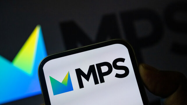 MPS logo on mobile device screen featuring green and blue geometric emblem in office atmosphere.