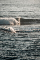 Naklejka premium Rolling ocean waves with cresting surf and shimmering soft sunlight reflecting on textured sea surface at calm horizon