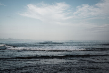 Obraz premium Moody coastal seascape with gentle waves, overcast sky and distant horizon, soft muted tones and textured ocean surface