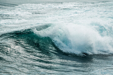 Naklejka premium Close-up of a turbulent teal ocean wave breaking with white foam and dynamic spray over choppy textured seawater