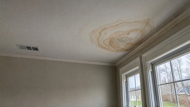 Brown water stain spreading across a suburban ceiling - insurance claim - copy space