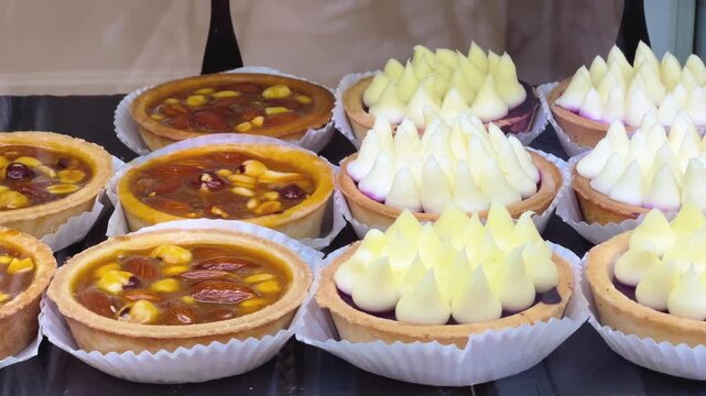 Assorted gourmet tartlets with glazed nuts and white cream in a bakery display case, food industry and cafe, sweet dessert menu.