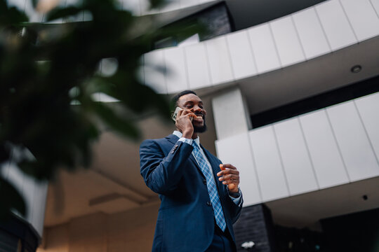 Black businessman communicating on smartphone near modern building