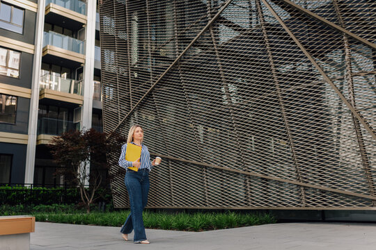 Professional woman walking downtown holding folder and coffee