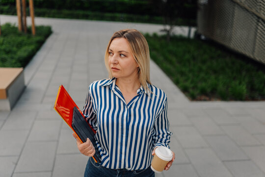 Businesswoman walking outdoors holding documents and coffee