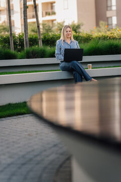 Woman working remotely outdoors with laptop and coffee