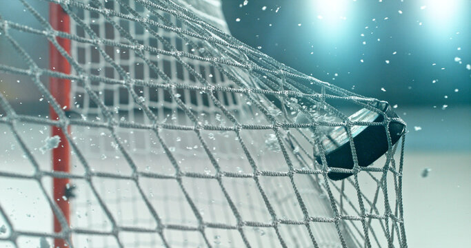 Action sports photo of a hockey puck flying into the goal net during a scoring shot, with ice particles in the air, capturing speed and intensity.