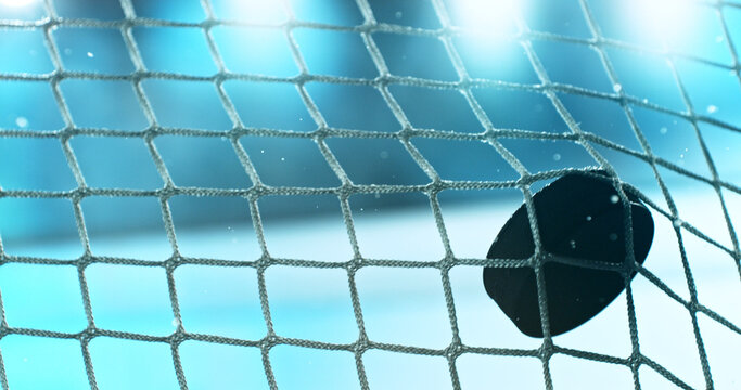 Action sports photo of a hockey puck flying into the goal net during a scoring shot, with ice particles in the air, capturing speed and intensity.