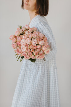 Studio portrait featuring brunette in blue gingham dress embracing large arrangement of pink roses