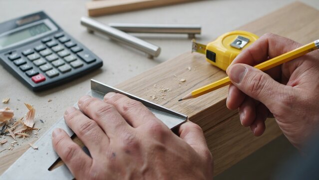 Craftsman marking wooden plank using metal square tool and yellow pencil for precise carpentry measurement with while working project close person using