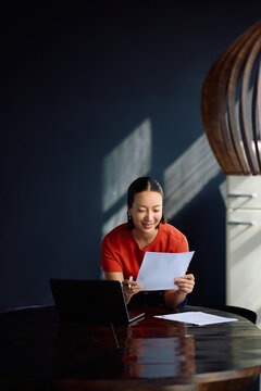 Happy Korean woman going through paperwork while working at home.