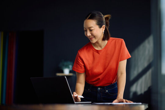 Smiling Korean woman working on laptop at home.