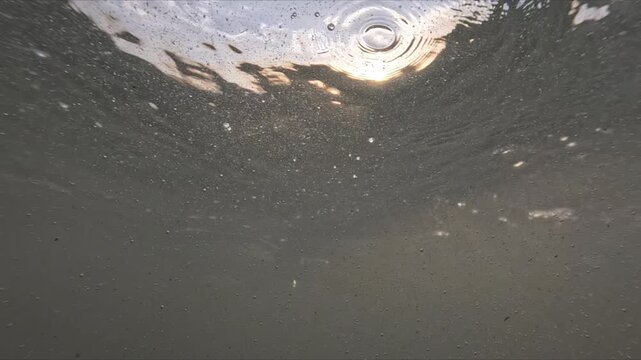 Split level ocean footage shows waves above and below water with air bubbles and droplets in golden sunset light