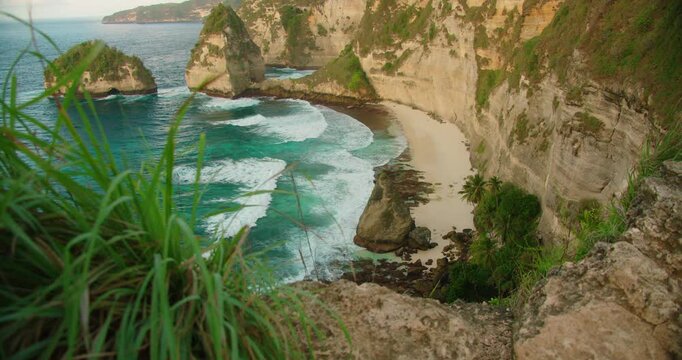 Jagged cliffs border the clear blue water and white sand of Diamond Beach in Nusa Penida Indonesia