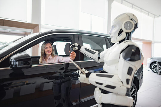 A futuristic robot interacts with a woman inside a car at a modern dealership, showcasing advanced technology in sales