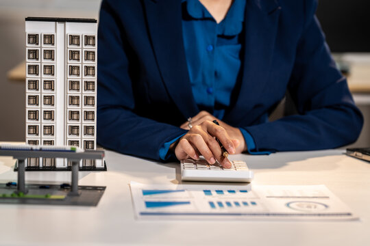 Business person working at desk with building model, calculator, and charts for real estate or financial planning