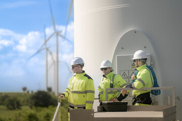 Fototapeta premium Three wind farm technicians stand talking at the open door in the base of a turbine tower, the curved white wall of the shaft rising behind them into the bright summer sky
