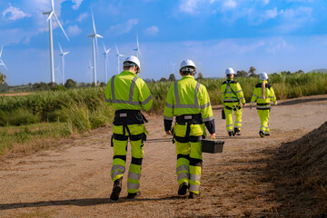Fototapeta premium A maintenance team walks away down a long dirt track that runs between rows of wind turbines, the leading pair close together and two more figures following far behind