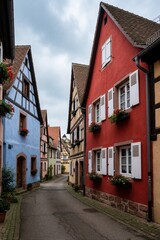 Fototapeta premium Colorful historic Alsace street lined with half timbered houses and red painted home. Cobblestone path leads past ancient town buildings with flower boxes.