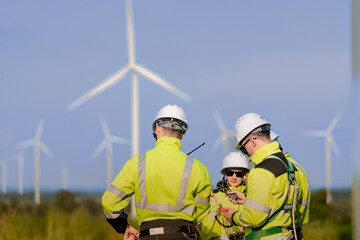 Fototapeta premium A small wind farm crew checks a handheld wind meter together in the late light, one man's arm crossing the frame to hold the probe while a colleague watches from behind