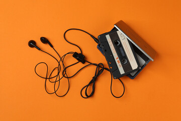 Retro portable cassette player with headphones and audio cassettes on an orange background.  © Pixora ST 
