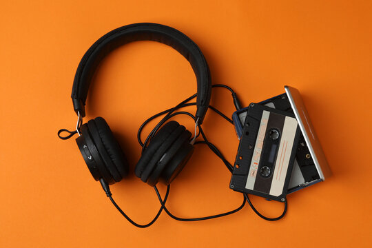 Retro portable cassette player with headphones and audio cassettes on an orange background.
