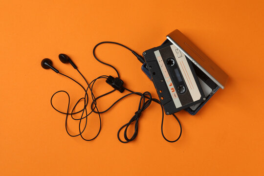 Retro portable cassette player with headphones and audio cassettes on an orange background.
