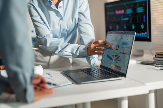 Business team collaborating, analyzing charts and graphs on a laptop screen, discussing financial data for strategy