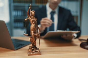 Lady Justice statue standing on a desk with a blurred lawyer in a suit working on legal documents...