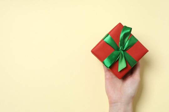Woman's hand holding gift box with green satin ribbon bow on pastel background, space for text. Top view
