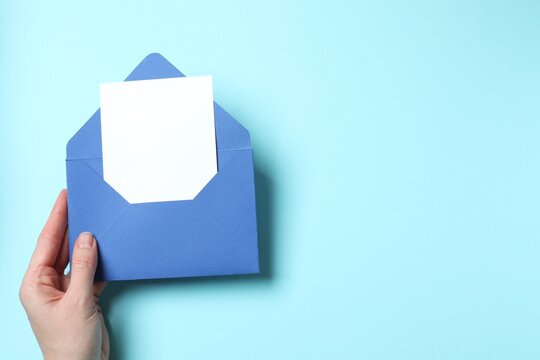 First person top view photo of girl's hand holding blue paper envelope with white card on pastel blue background with blank space