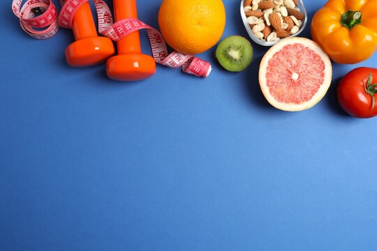 Weight loss concept. Top view photo of fruits, vegetables, nuts, tape measure and dumbbells on blue background with blank space